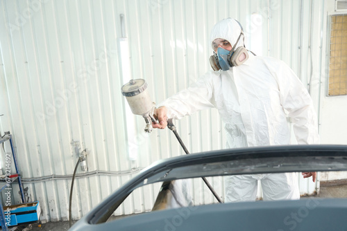 Skilled auto repair shop worker is painting motor vehicle body panel