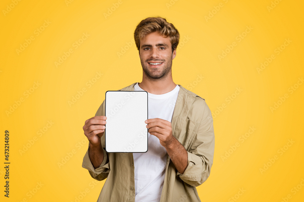 European man displays tablet with blank screen, yellow backdrop European man displays tablet with blank screen, yellow backdrop