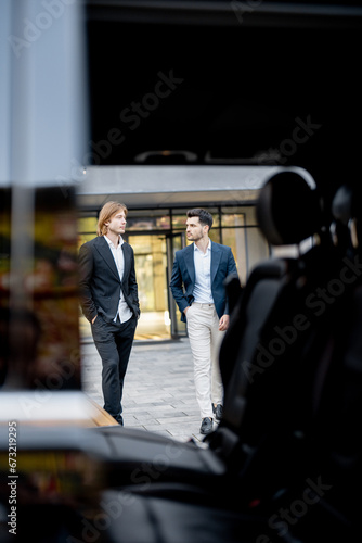 Two businessmen walk to the car from a building, view through a vehicle door. Concept of business transportation