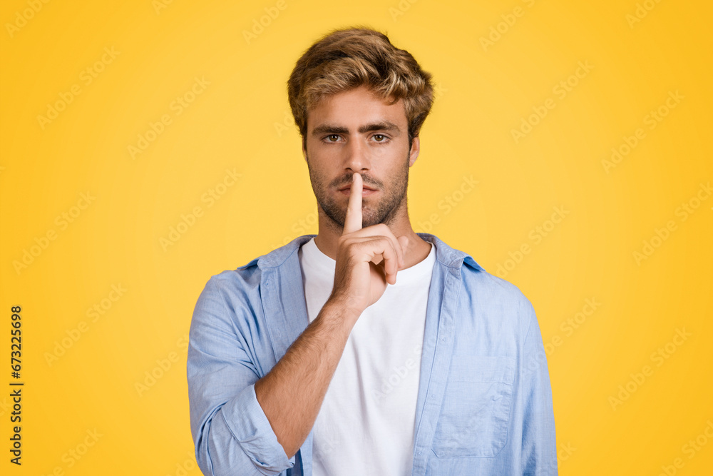 Serious european man gesturing silence on yellow backdrop - obrazy, fototapety, plakaty 