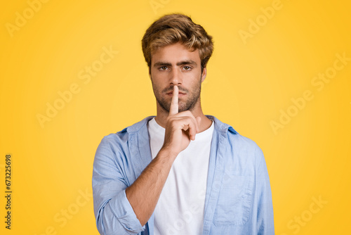 Serious european man gesturing silence on yellow backdrop