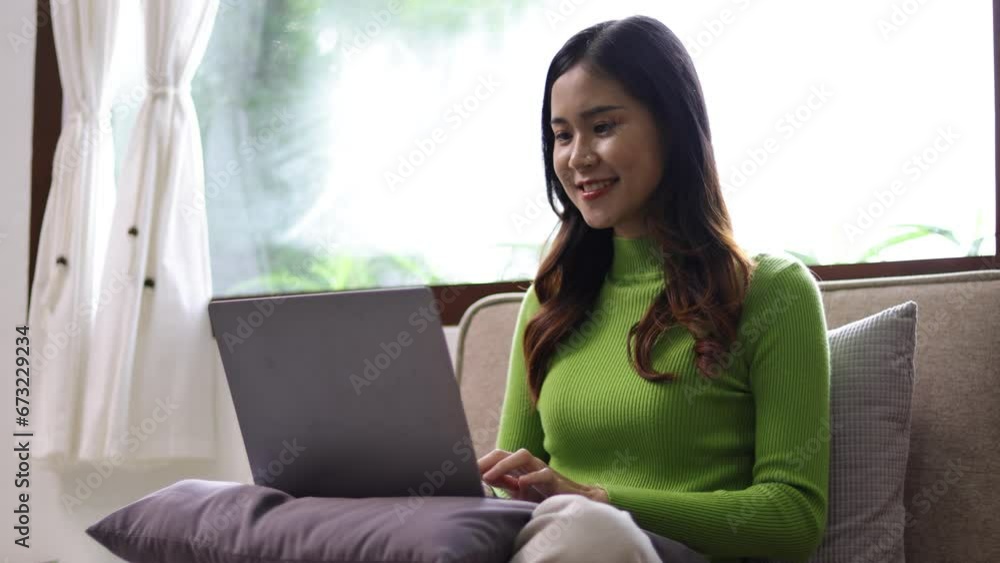 Young Asian woman at home relaxing on the sofa in the living room, she is happily using her laptop. Young Asian woman at home relaxing on the sofa in the living room, she is happily using her laptop.