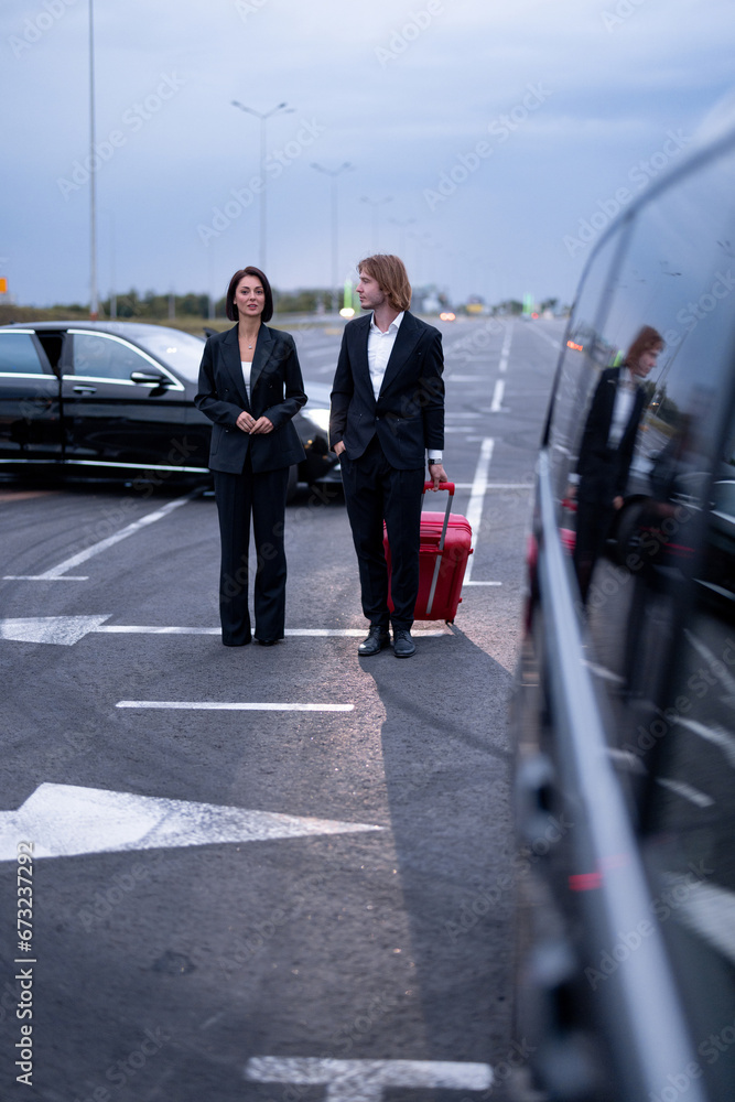 Business couple walking with a suitcase on parking lot, arrived by luxury taxi. Concept of transportation and business trips