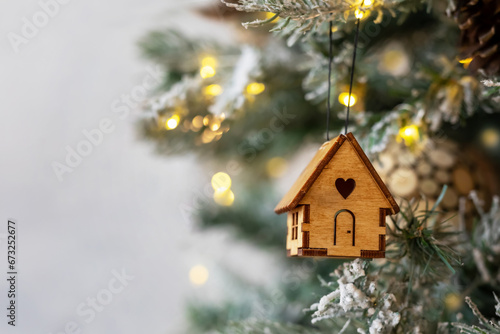 Christmas tree toy in the form of a house on a branch. Concept house insurance, house gift. Christmas mood background. Family budget. Mortgage buying real estate.