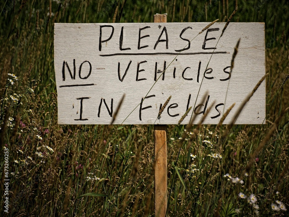 Sign that reads 'Please No Vehicles In Fields' against a backdrop of a lush, vibrant field