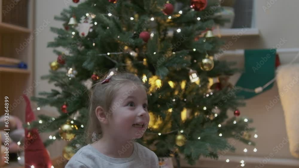 Excited curious little girl smiling, opening christmas gifts. Beautifully decorated christmas tree and house with lights and lantern. Excited curious little girl smiling, opening christmas gifts. Beautifully decorated christmas tree and house with lights and lantern.