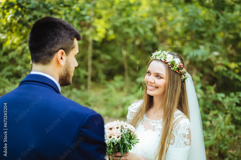 happy newlywed couple. the bride stands with a bouquet in her hands in a white dress, the groom in a blue business suit, a young couple walking through the forest