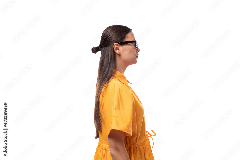 European young woman with black hair dressed in an orange summer dress stands sideways European young woman with black hair dressed in an orange summer dress stands sideways