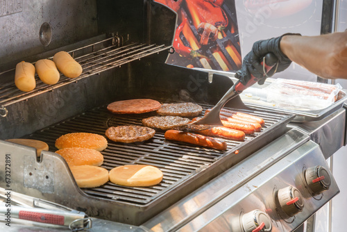 Process of cooking meat for burgers and cheeseburgers, sausages for hot dogs, buns on a grill with burning coals. Street food