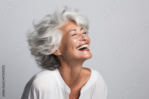senior woman in 60s age with grey hair portrait smiling and laughing with grey background photo