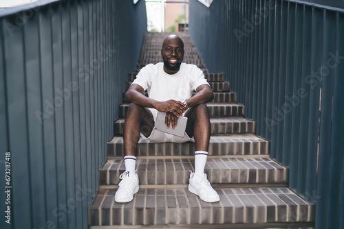 Stylish black man sitting on stairway while looking at camera