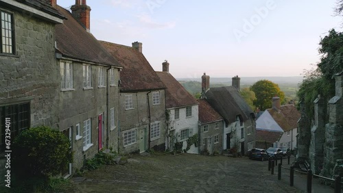 Gold Hill Shaftesbury.  Location of iconic Hovis Bread commercial by Ridley Scott. Evening sunshine on a summers day, steep cobbled street in England.   Drone tracks up the hill. No. 2 of a set of 6. photo