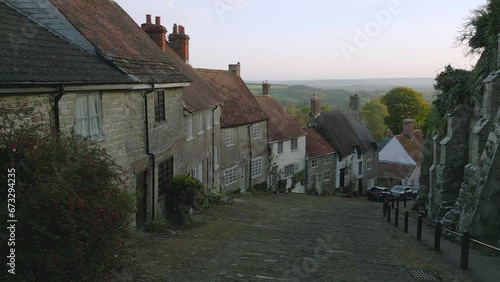 Gold Hill Shaftesbury England.  Location of iconic Hovis Bread commercial by Ridley Scott. Evening sunshine on a summers day, steep cobbled street in England.  Drone tracks up the hill.  No.1 of 6. photo