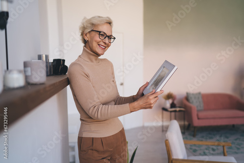 Cheerful senior woman holding photo frame in living room