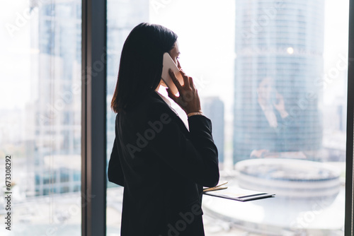 Serious businesswoman talking on smartphone near glass wall in office Free Download Serious businesswoman talking on smartphone near glass wall in office - GFXLoad