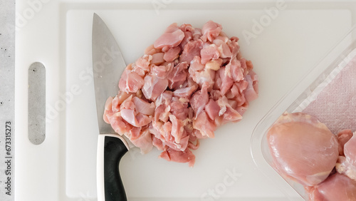 Chopped raw chicken fillet close-up on a white plastic cutting board