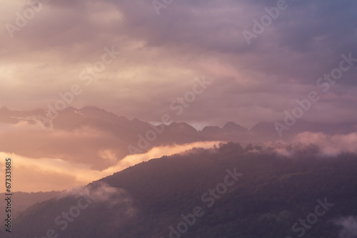 Fog and clouds in the mountains against the backdrop of the setting sun, changeable weather in the mountains, clouds and nebula on mountain peaks