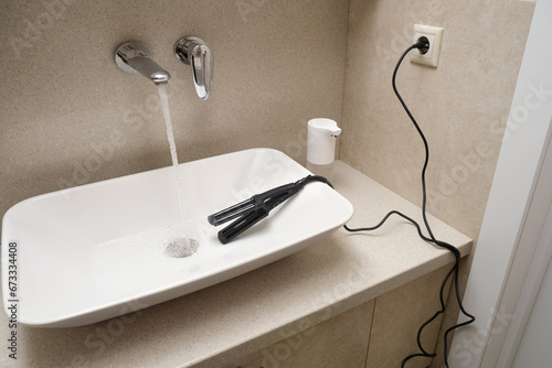 An electrical appliance lies dangerously in a sink with running water. Electrical shock can occur in the bathroom photo