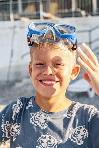 Handsome smiling boy with diving mask on head rests on beach closeup. Little child with scuba equipment for underwater swimming at resort