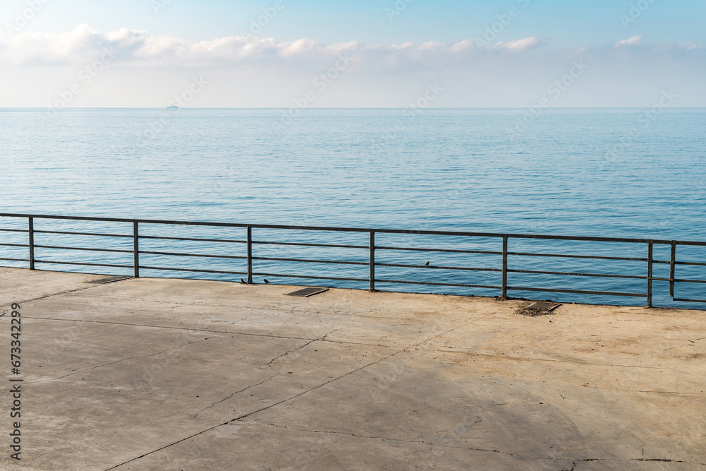 Empty concrete ground with metal railings over calm sea on sunny day. City embankment and tranquil azure bay at resort. Travelling in summer