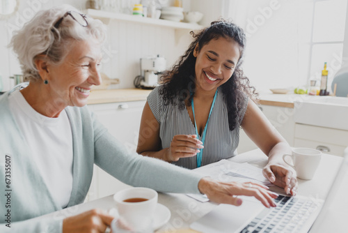 Side view of young black female volunteer social worker teaching senior caucasian lady how to use laptop, wireless internet, browsing web pages, reading news, showing her new skills photo
