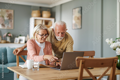 Senior couple sit at a table in the living room with laptop,working from home office
