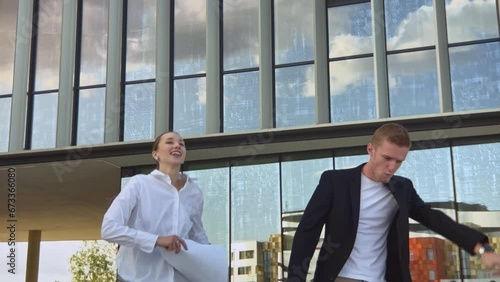 Happy positive business people man and woman dancing jumping funny, throwing up to air paper documents celebrating success and achivements on city street. Slow motion, two persons photo