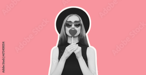Portrait of beautiful young woman with lollipop blowing her lips with lipstick sending sweet air kiss wearing heart shaped sunglasses, black round hat on pink background, black and white photo