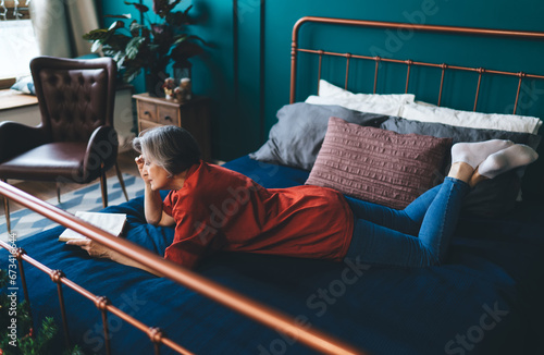 Mature woman reading book on bed with pillows