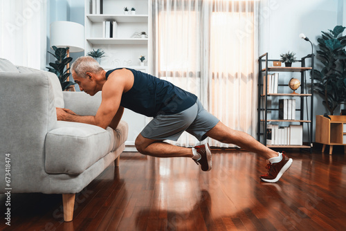 Active and fit senior man warmup and stretching using furniture before home exercising routine at living room. Healthy fitness lifestyle concept after retirement for pensioner. Clout