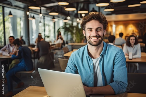 In a modern office setting, a young businessman smiles while collaborating with colleagues, showcasing teamwork and creative success.