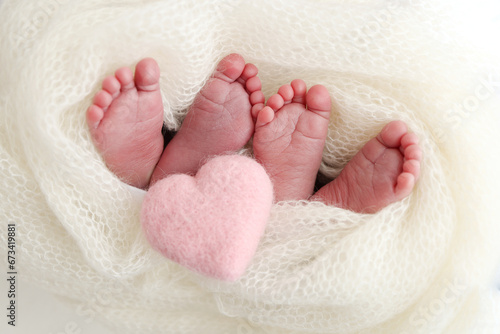 Feet of newborn twins. Two pairs of baby feet in a white knitted blanket. Pink knitted heart. Close up - toes, heels and feet of a newborn. Newborn brothers, sisters. Studio macro photography. 