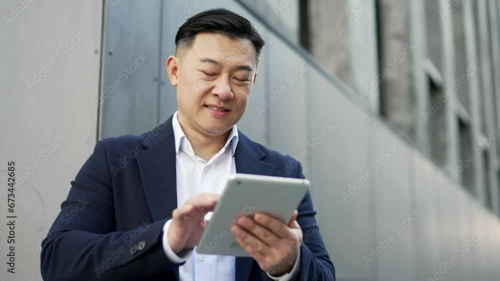 Close up. Businessman in formal suit is using tablet while standing on street near an office building. Happy entrepreneur reads writes email message or chats online with a business partner or friend Close up. Businessman in formal suit is using tablet while standing on street near an office building. Happy entrepreneur reads writes email message or chats online with a business partner or friend