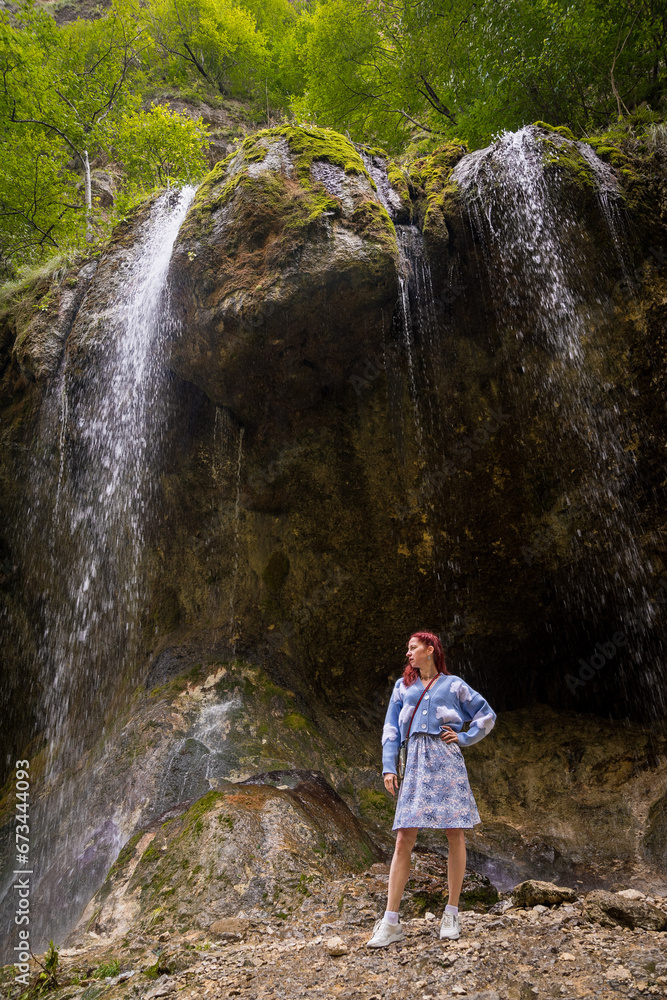 Young girl in blue dress standing under beautiful Chegem waterfalls, Caucasus, Russia