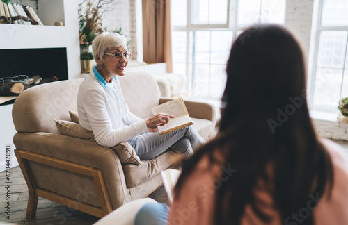 Senior woman sitting on sofa and reading book at home
