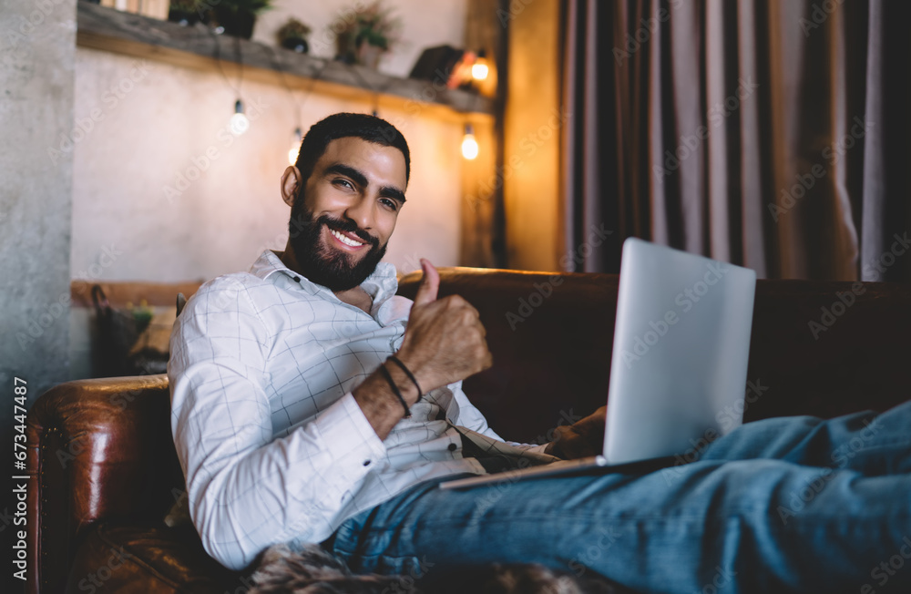 Man with laptop sitting on sofa and showing approve gesture