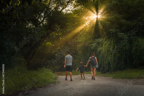 Small family walking down a hill at sunset with sun rays illuminating them © Malena Gonzalez