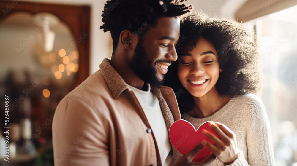Smiling afro american couple hugging each other and holding a card given for Valentine's Day. Relationship concept - obrazy, fototapety, plakaty 