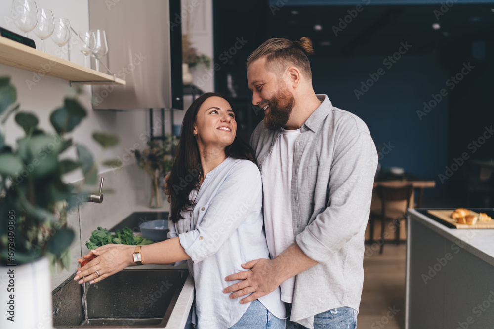 Happy couple hugging and washing vegetables in kitchen Happy couple hugging and washing vegetables in kitchen
