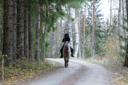Reaper riding on gravel road in Autumn scenery. Ghost rider. Icelandic horse. Halloween. © AnttiJussi