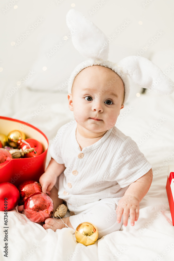 Christmas Baby Child holding christmas bauble near Present Gift Box over Holiday Lights background Christmas Baby Child holding christmas bauble near Present Gift Box over Holiday Lights background