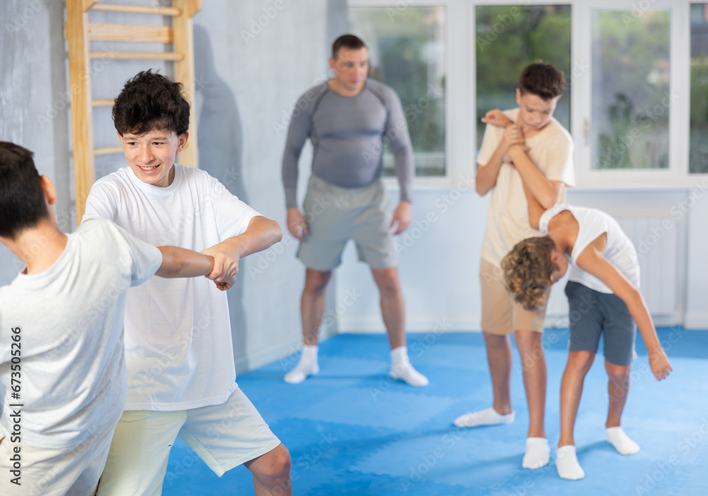 Fototapeta premium Concentrated teen boys practicing basic protection skills in training bout during self defense course in gym under guidance of instructor