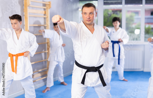 Karate master supervising formation of teenage practitioners in kimonos, demonstrating hand strikes and martial arts skills during group kata..