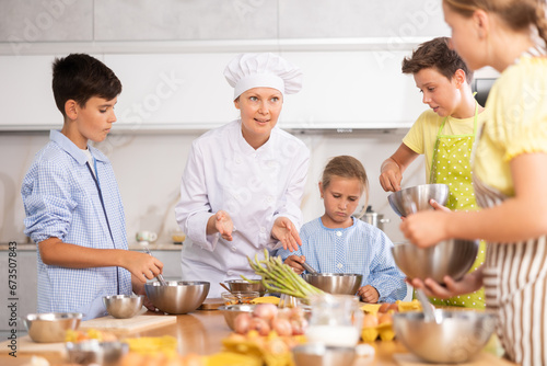 Adult woman chef at master class teaches group of children how to cook food