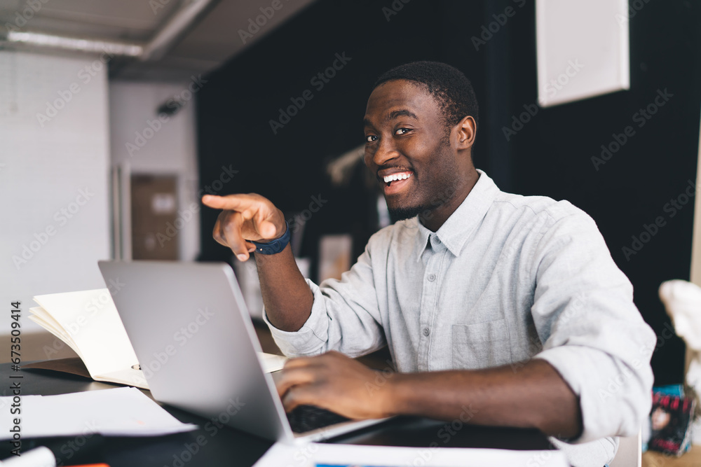 Cheerful black man smiling and pointing during work Cheerful black man smiling and pointing during work