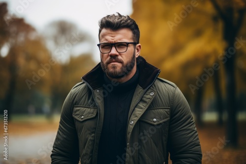 Handsome bearded man in a stylish jacket and glasses is standing in the autumn park.