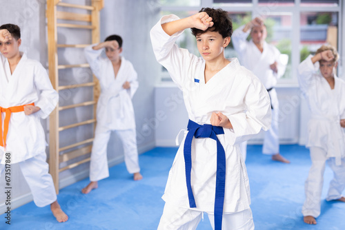 Concentrated teenager in white kimono practicing punches in gym during group martial arts workout. Shadow fight, combat sports training concept ..
