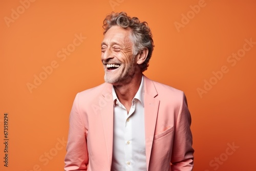 Portrait of happy senior man in pink suit on orange background.