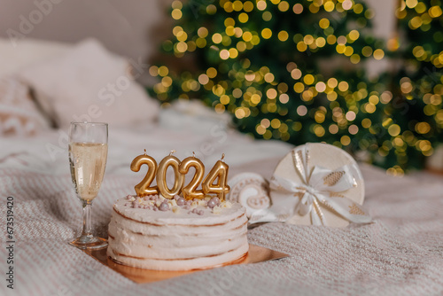 a cake with 2024 candles in Christmas decorations. A glass of champagne. Preparations for family dinner, home recipes, cooking chocolate cake. beige golden background