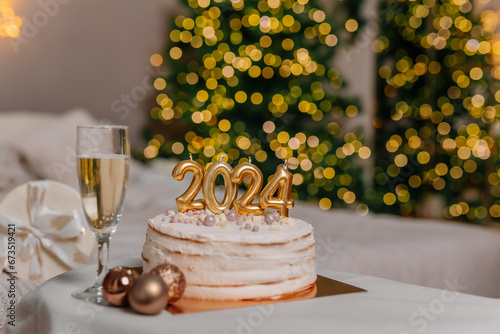 a cake with 2024 candles in Christmas decorations. A glass of champagne. Preparations for family dinner, home recipes, cooking chocolate cake. beige golden background